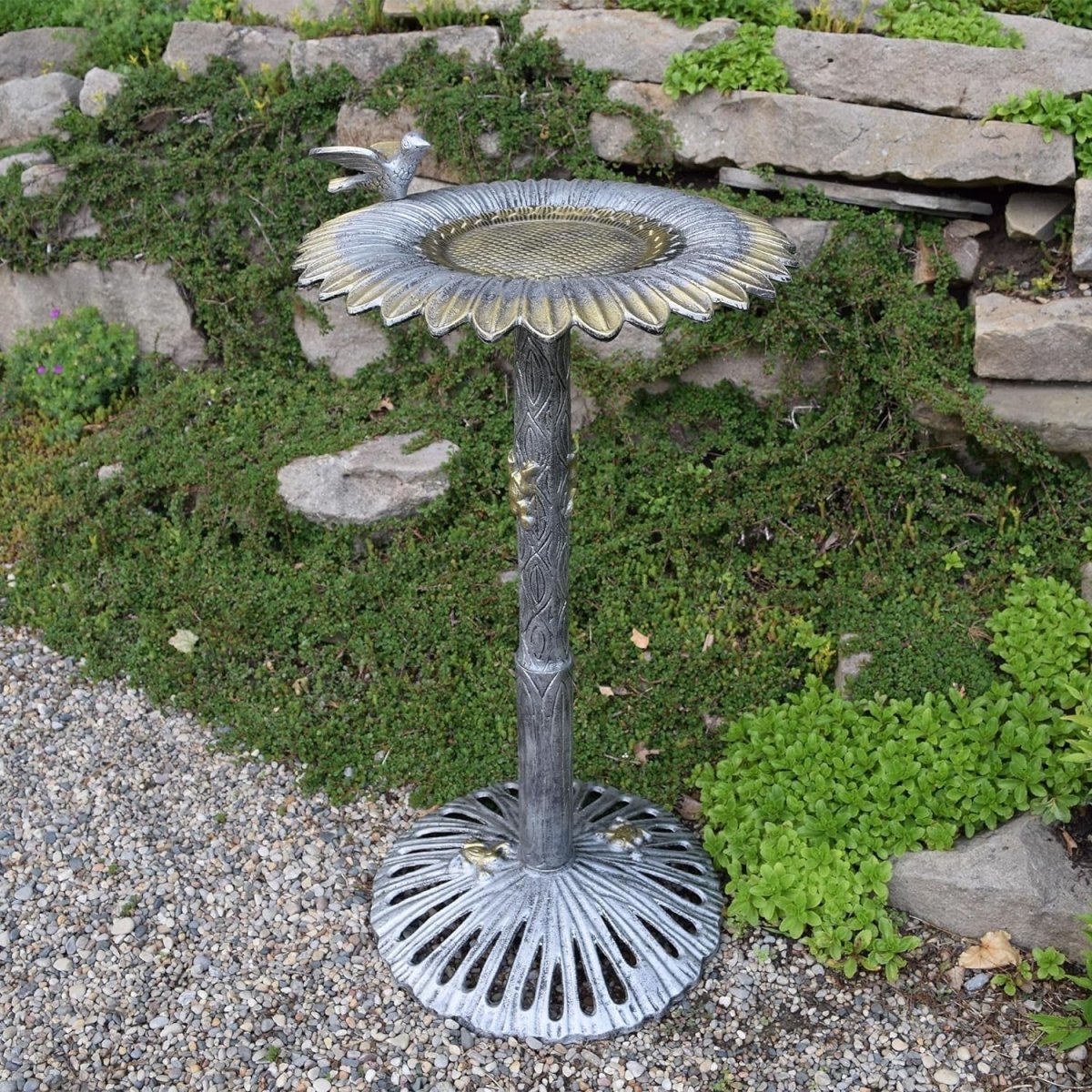 Decorative metal bird bath with sunflower design in a garden setting