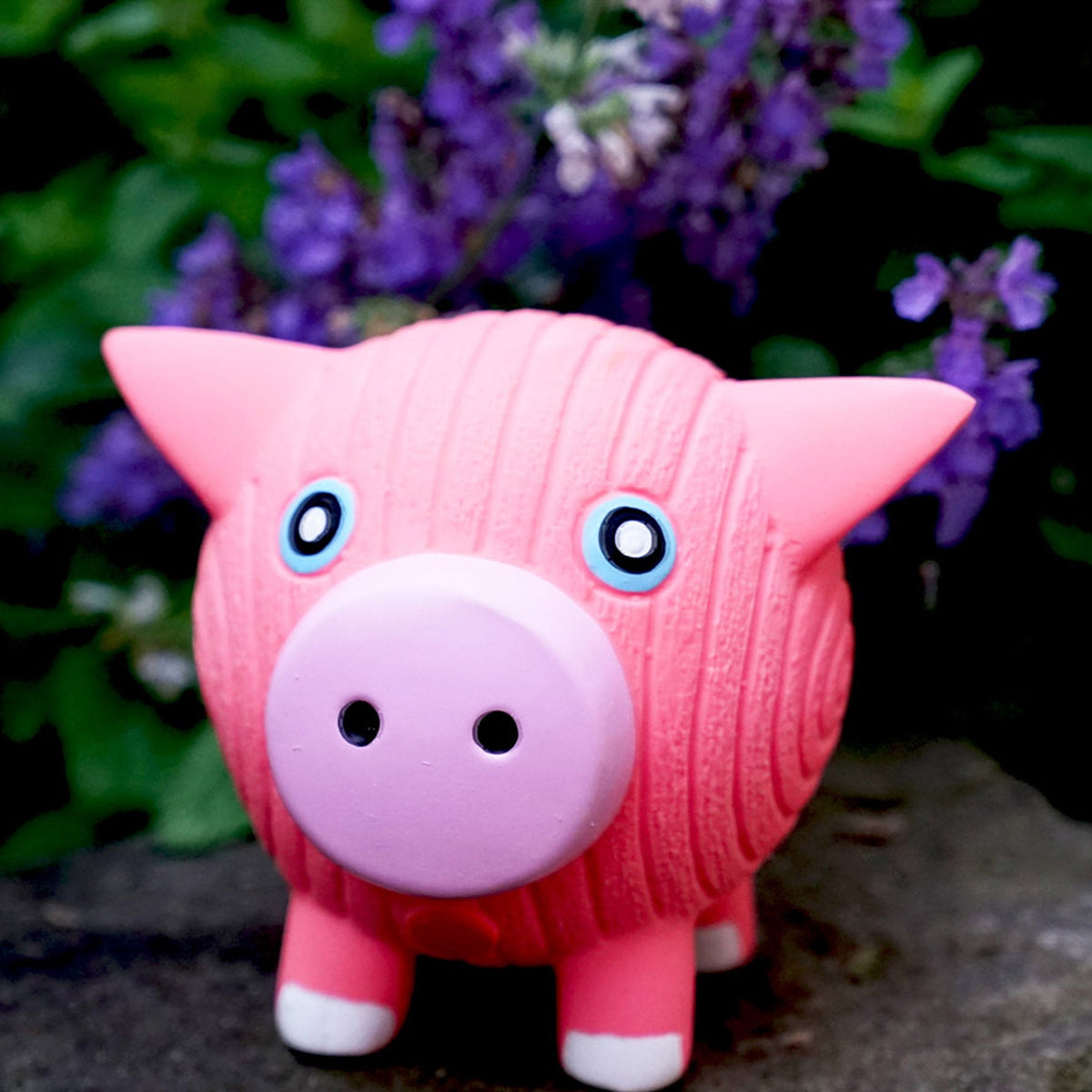 Pink piggy bank with blue eyes in front of purple flowers