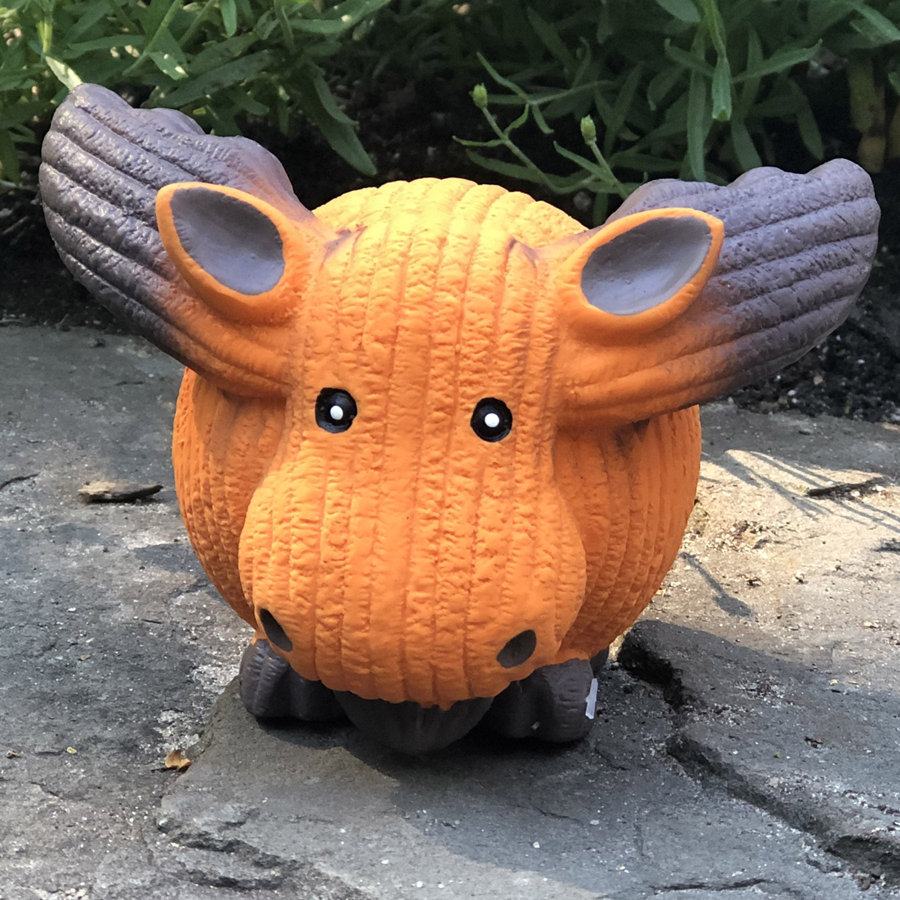 Orange and gray toy hippo on a stone surface with greenery in the background