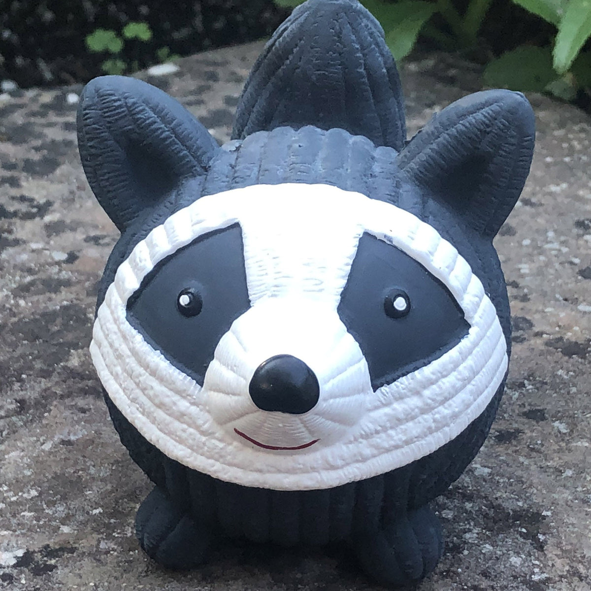 Plush raccoon toy on a stone surface with greenery in the background